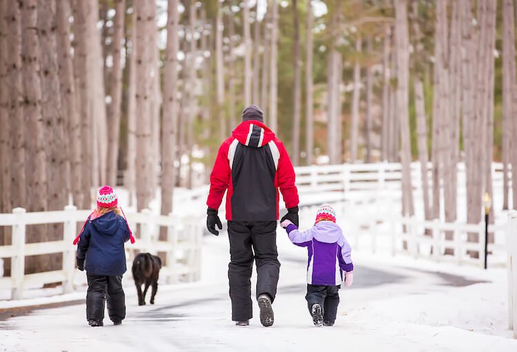 Two young girls walking with Dad down a scenic driveway in winter.